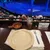 An empty dining table is set with a plate, bowl, drink, and fork, overlooking a theater stage with an audience seated below.