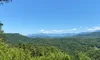 A black ATV is parked on a mountain trail with a scenic view of lush green hills and a clear blue sky in the background.