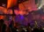 The image depicts an indoor setting designed to resemble a theatrical pirate ship, complete with sails and rigging, where people are seated at tables watching an event.
