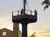 The image shows a pirate ship's lookout post with figures of pirates at sunset, surrounded by themed architecture and palm trees.
