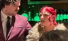 A man in a suit and a woman with red hair and a fur stole are engaging in conversation in a bar setting.