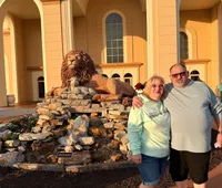 Three people are standing in front of a building with large arches, next to a lion sculpture on a rock display.