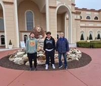 Three people are standing in front of a building with large arches, next to a lion sculpture on a rock display.