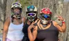 Three people in helmets pose together in front of an ATV in a wooded area.