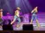 Performers wearing cowboy hats and denim outfits are singing and dancing on a stage under bright lights.