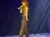 A performer in a red cowboy hat and sparkly outfit sings into a microphone on stage under dramatic lighting.