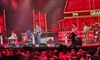 A band is performing on stage at the Grand Ole Opry with red lighting and a crowd watching.