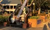 A large black guitar sculpture with autographs stands outdoors in front of a building, surrounded by potted plants and trees.