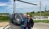 Two women stand smiling with thumbs up in front of a helicopter, with a pilot visible inside.