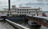 A large paddlewheel riverboat docked at a pier under a partly cloudy sky.