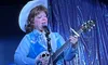 A person in a blue and white western outfit is performing on stage, playing a guitar and singing into a microphone.