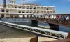 The image shows a large paddlewheel steamboat docked by a pier under a partly cloudy blue sky.