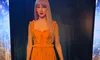 A female figure in a flowing orange dress is holding a microphone against a starry background.