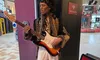 A wax figure of a musician is displayed with a guitar at Madame Tussauds, inside a commercial building.