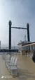 The image shows a deck of a large boat or ship with white wooden chairs lined up in rows and two tall decorative smokestacks in the background.