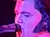 A musician is performing on stage with a guitar, illuminated by purple and blue stage lights against a backdrop with small star-like lights.