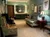 A cozy room with floral armchairs, a cushioned sofa, wall art, a dressing table, and a decorative ceiling light.