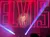A performer in a white suit sings on stage, illuminated by red and purple lights, with the large word 