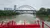 A red paddlewheel boat is moving down a river towards a modern arched bridge, with city buildings in the background.