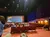 A theater with an audience facing a large screen displaying an advertisement, surrounded by a decor resembling stone arches.