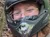 A person wearing a helmet is sitting on an ATV and waving in a wooded area.