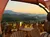 A scenic outdoor patio with wooden chairs and tables overlooks a mountainous landscape at sunset, under triangular shade canopies.
