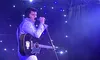 A performer in a sparkling suit sings on stage with a guitar under starry lights.
