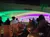 People are seated on a boat traveling under a bridge adorned with colorful lights.
