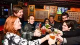 A group of cheerful people are toasting with drinks in a lively bar setting.