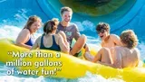 A group of friends is laughing and enjoying a sunlit ride down a water slide in a yellow raft.