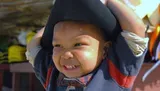 A joyful baby with a wide smile is wearing a large black hat.