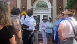 A group of people is attentively listening to a man speaking in front of the Alexandria Library's Kate Waller Barrett Branch.