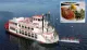 A traditional paddlewheel riverboat is cruising on calm waters under a clear sky.