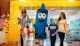 A family is enjoying a fun outing with two people in crayon costumes at a colorful, playful location.