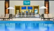 The image features a serene poolside area with loungers and a bar called Bywater Pool Deck & Bar, where an attendant is present behind the counter.