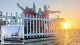 A group of people is posing happily behind a white picket fence on a waterfront at sunset.