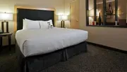 The image shows a neatly arranged hotel room with a large bed, nightstands, lamps, and a decorative mirror reflecting an image on the opposite wall.