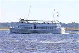 A passenger boat sails on a body of water with a few people visible on the upper deck.