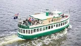 A group of passengers is enjoying a scenic boat tour on a green and white riverboat flying the American flag.