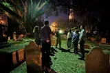 A group of people is standing in a cemetery at twilight, possibly on a guided tour, as one person gestures and appears to be telling a story or giving information.