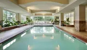 The image shows an indoor swimming pool area with lounge chairs and large windows letting in natural light.