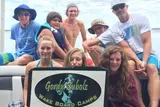 A group of people, likely from a wakeboarding camp, are posing for a photo with a sign that says Gordy Bubolz Wake Board Camps, suggesting a fun day on the water.