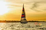 A sailboat with a colorful sail glides over the water against a stunning sunset backdrop.