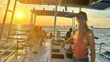 A group of people are enjoying a sunset cruise on a boat with a view of the distant city skyline.