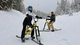 Two people are having fun riding snow bikes down a snowy mountain slope.