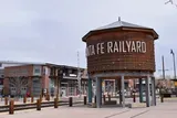 The image shows the Santa Fe Railyard area with a large vintage wooden water tower featuring the text Santa Fe Railyard in a modernized urban setting with clear skies overhead.
