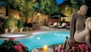 An elegant outdoor pool area is adorned with lush plants, flowers, and a large sculpture, creating a serene evening atmosphere.