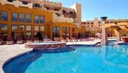 The image shows a bright and sunny pool area with loungers and a Southwestern-style hotel building in the background.