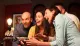 Four people are excitedly gathered around a mysterious, vintage-looking device, with expressions ranging from amazement to amusement.