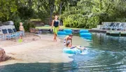 A family enjoys a sunny day at a lazy river, with children playing in the water and an adult supervising.